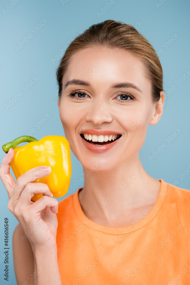 happy young woman with natural makeup posing with bell pepper isolated on blue happy young woman with natural makeup posing with bell pepper isolated on blue