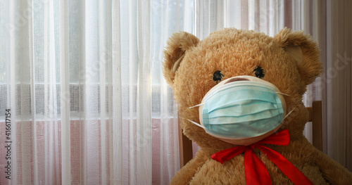 Teddy Bear wearing medical mask to emphasize the social aspect of self isolation and loneliness that happens when one is alone, lonely teddy bear. Panorama coronavirus covid-19 global pandemic Banner © Nodi
