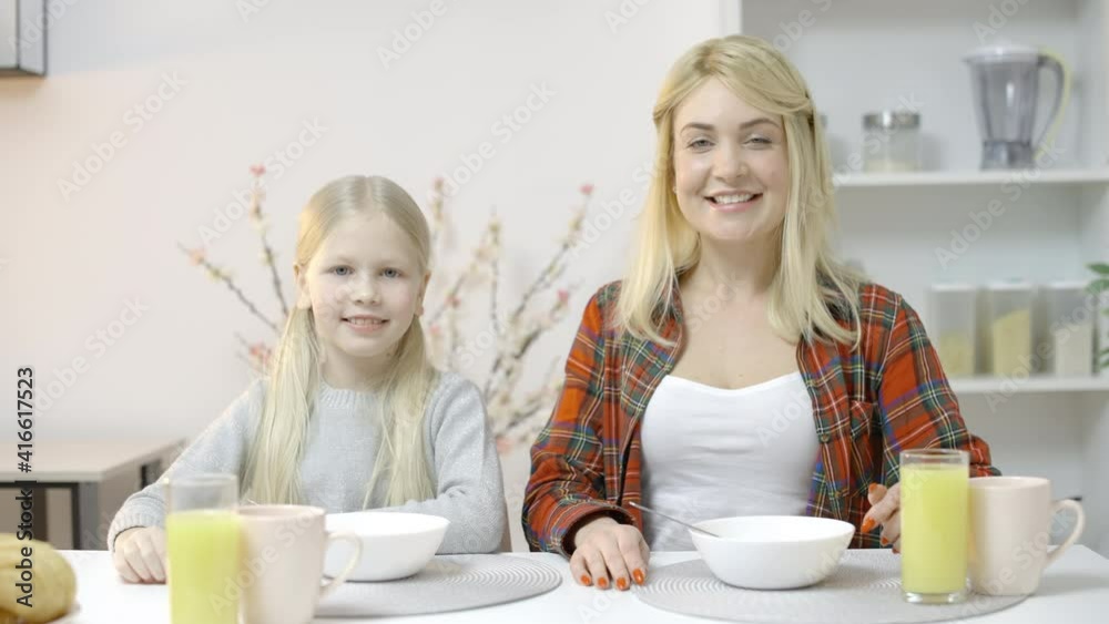 Cheerful daughter and mom sitting at kitchen table, smiling, family relationship Cheerful daughter and mom sitting at kitchen table, smiling, family relationship