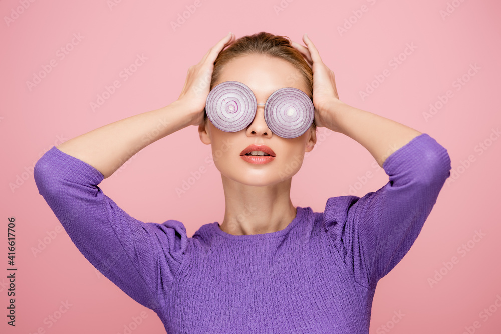 young woman touching head while posing in eyeglasses with onion rings isolated on pink, surrealism concept