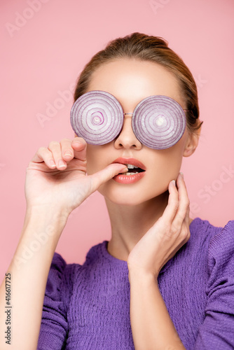 sensual woman in eyeglasses with purple onion rings, biting thumb isolated on pink, surrealism concept © LIGHTFIELD STUDIOS