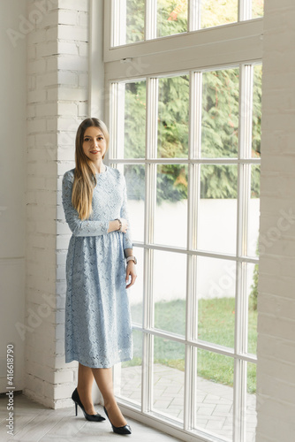 Attractive young girl near the window in a blue dress