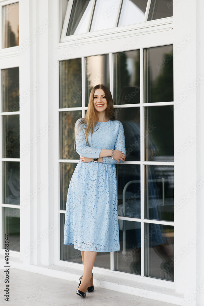 Attractive young girl on the background of the white house in a blue dress Attractive young girl on the background of the white house in a blue dress