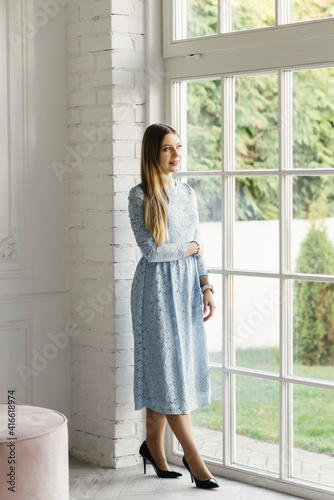 Attractive young girl near the window in a blue dress