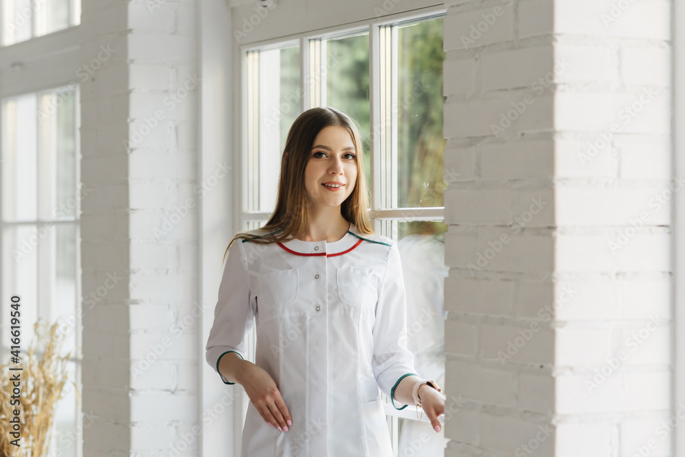 Fototapeta premium Attractive young girl in a white medical gown in a beautiful interior, VIP clinic, beauty and relaxation salon