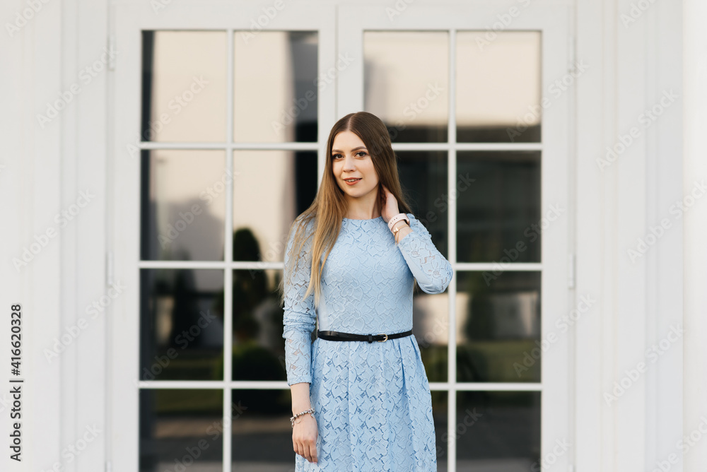 Attractive young girl on the background of the white house in a blue dress Attractive young girl on the background of the white house in a blue dress