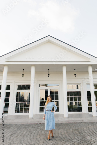 Attractive young girl on the background of the white house in a blue dress
