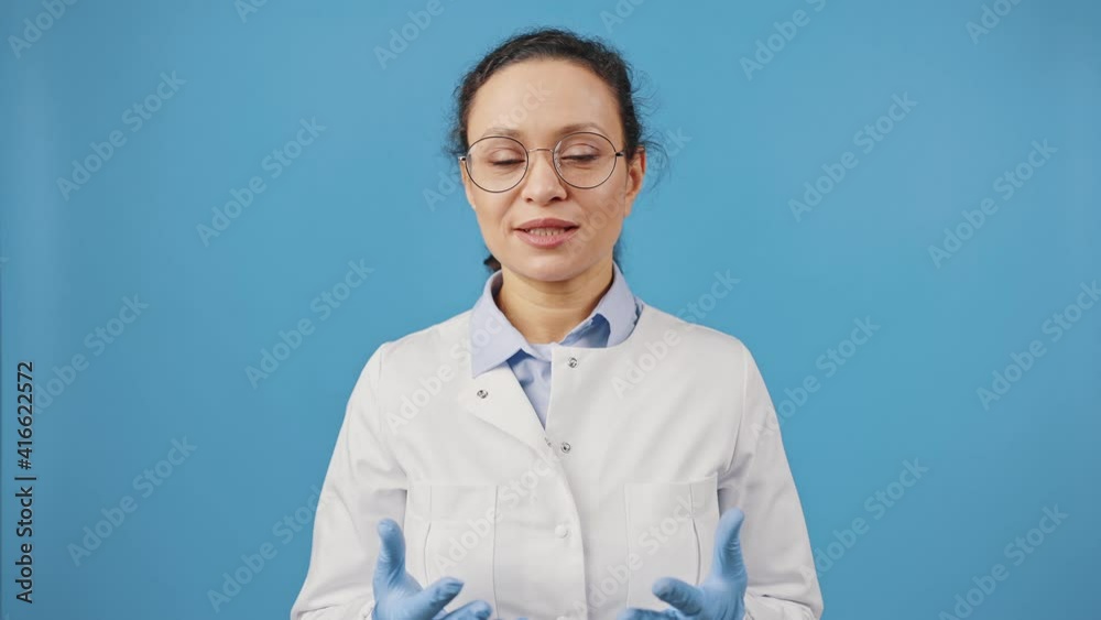 Studio portrait of woman doctor in eyeglasses talking to camera, recording video blog