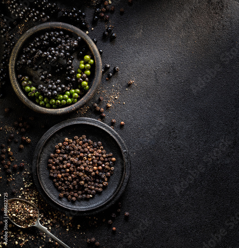 Black pepper in various forms; raw, dried and crushed peppercorns on a black background with space for text