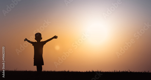 Happy child feeling positive with arms up to the sunset sky. 