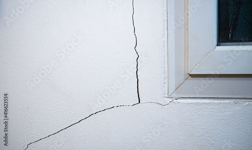 Cracks on the wall. The crack in the cement wall at the window sill, caused by the subsidence of the ground, causing a slit at an oblique angle. photo