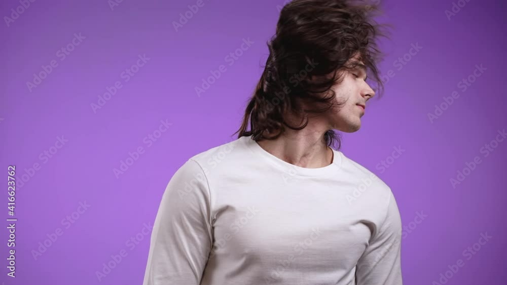 Handsome man with long curly hair having fun, dancing head, gets high from music, smiling in studio against violet background. slow motion Handsome man with long curly hair having fun, dancing head, gets high from music, smiling in studio against violet background. slow motion