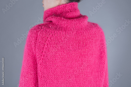 Close up of yang woman in hot pink sweater. Back view. Grey background.