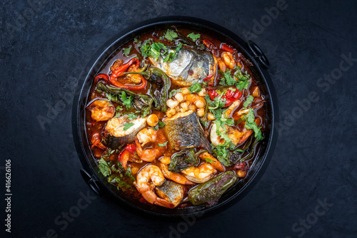 Modern style traditional Mexican seafood pozole soup with fish, king prawns and hominy in a clear sauce served as top view in design pot