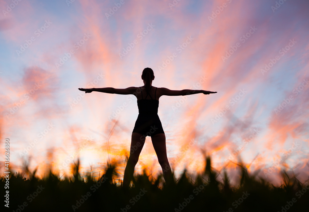 Body balance and health. Strong fit healthy woman silhouette doing stretching exercises outdoors at sunset. 