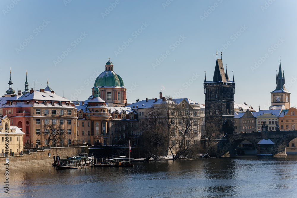 Dome of baroque vhurch of St Francis of Assisi, Old town bridge tower and water tower with clock and Medieval Charles Bridge, snow in sunny winter day, Prague, Czech Republic
