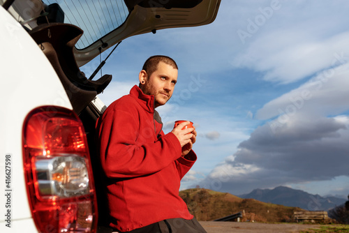 Young traveler man making a stop on his trip and enjoying a cup of coffee on the mountain at sunset. weekend getaways and active tourism.
