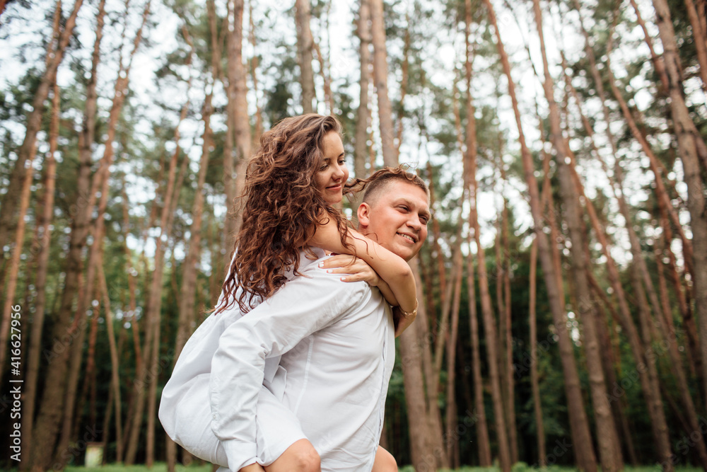 Smiling couple having fun in the park. Love and tenderness, dating, romance, lovers enjoy each other in the summer park. man carry on his back the beautiful curly hair woman smiling and laughing. Smiling couple having fun in the park. Love and tenderness, dating, romance, lovers enjoy each other in the summer park. man carry on his back the beautiful curly hair woman smiling and laughing.