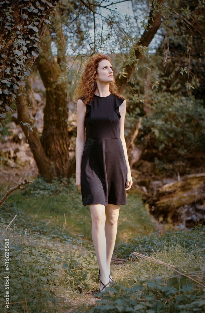 Curly girl wandering in the forest in a dark dress. Red hair woman walking in a mysterious atmosphere. Curly girl wandering in the forest in a dark dress. Red hair woman walking in a mysterious atmosphere.