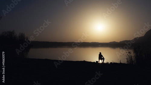 Fisherman on the shore of a lake at sunset