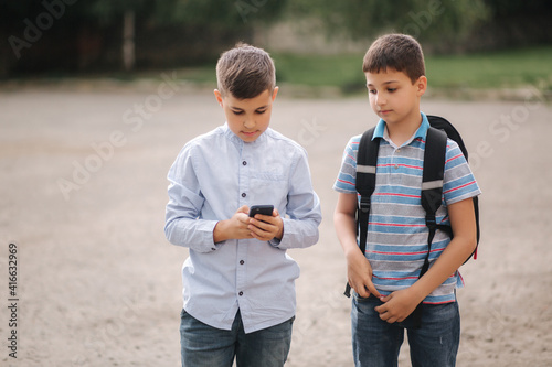 Two boys plays online games in quarantine. Young boys smile and use phone. One look how play another © Aleksandr