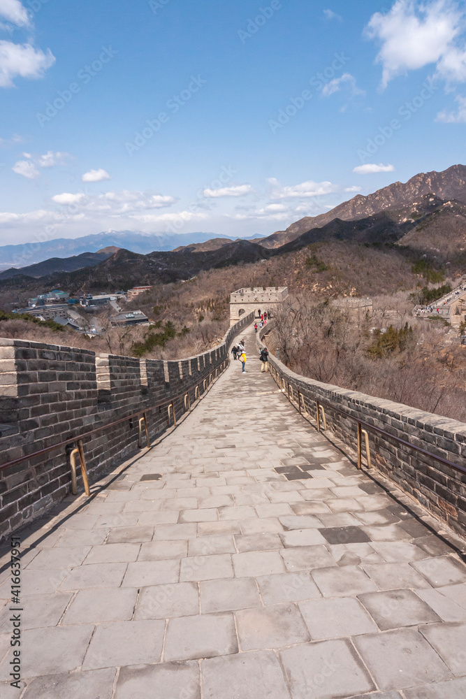 Fototapeta premium Beijing, China - April 28, 2010: Great Wall of China. Looking down on sloped walkway on top of wall which meanders over brown hills under blue cloudscape. Clothing adds bright colors.