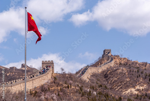 Beijing, China - April 28, 2010: Great Wall of China. Closeup of Chinese red flag with meandering wall in back under blue cloudscape.