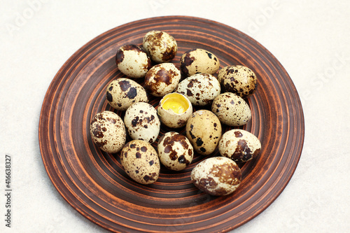 Small quail eggs in a clay plate on light stone background.
