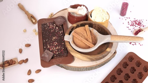 ingredients to make home chocolate, rotation on wooden board, cacao butter, coconut milk powder, cocoa powder, carob powder, nuts, nuts, dry berries, cinnamon sticks, chocolate bar, molds, 4K photo