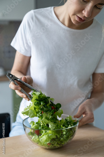 Close up of woman cooking vegetable salad at home kitchen. Female hands stirs vegetarian salad of fresh herbs and bell pepper, cherry tomatoes. Slimming diet. 