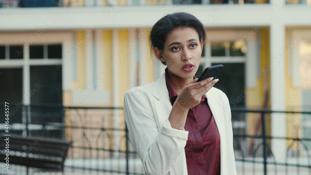 Fototapeta premium Focused mixed race woman making phone call outside. Lady talking on speakerphone