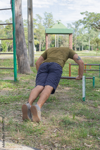 Hombre joven haciendo ejercicios de barra baja en ñu guazu luque asunción al medio día con mucho calor entre sombras  photo