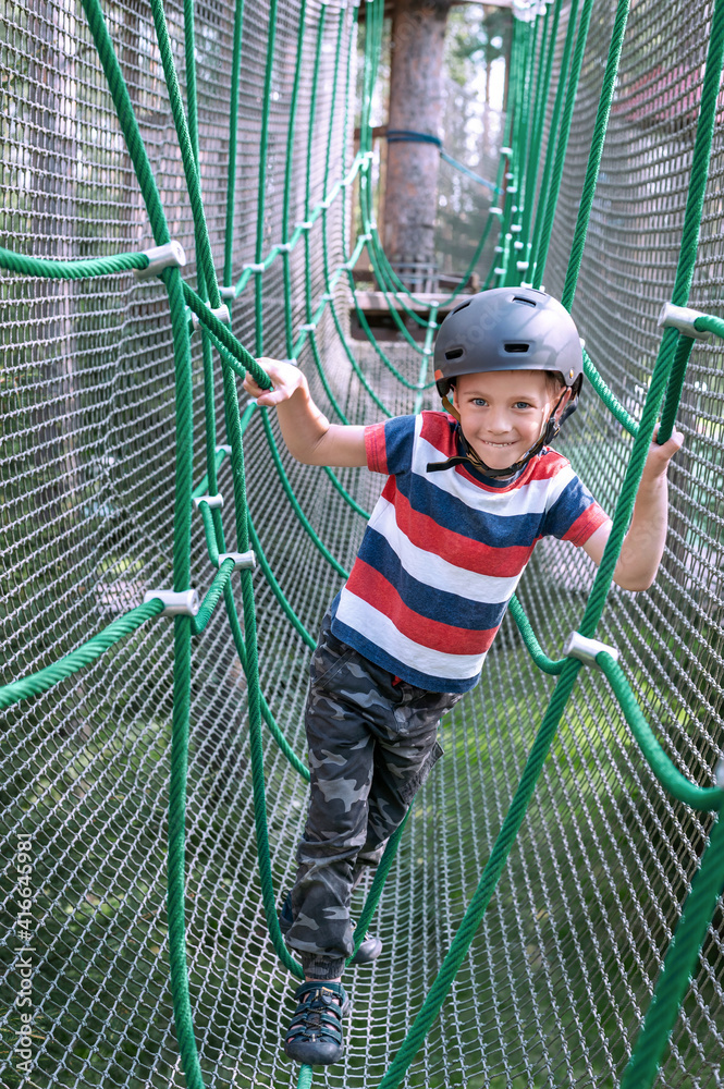 Little boy overcomes the obstacle in the rope park. Kid is climbing in rope attraction park. Little boy overcomes the obstacle in the rope park. Kid is climbing in rope attraction park.