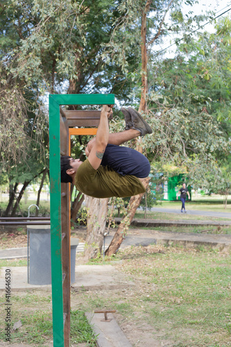 Hombre joven haciendo ejercicios de barras en ñu guazu luque asunción al medio día con mucho calor entre sombras  photo