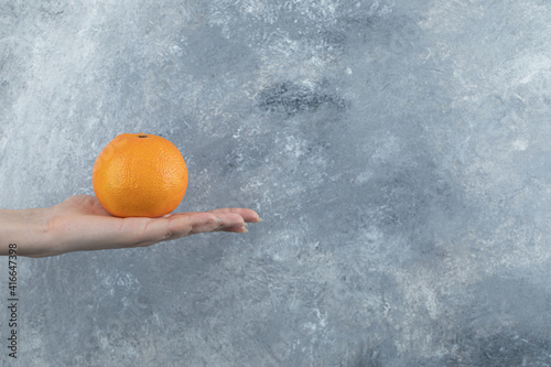 Female hand holding single orange on marble background photo