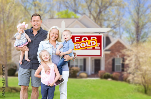 Happy Young Caucasian Family Outside In Front of Their New Home and Sold Real Estate Sign