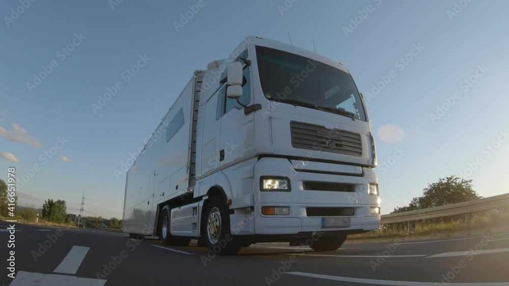 Cargo truck with cargo trailer driving on a highway. White Truck delivers goods in early hours of the Morning - very low angle drive thru close up shot.