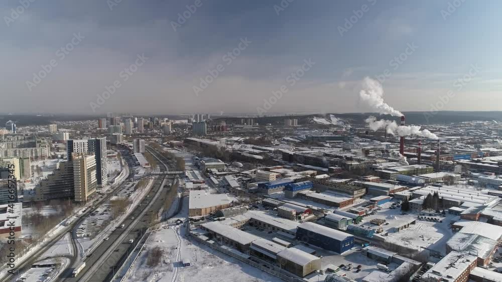 Aerial view of Highway with car traffic and Industrial Zone in the big city. Smoke (steam) is coming out of the chimneys. Nearby typical Soviet panel houses and modern multi-storey buildings. It's sno