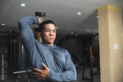 Photos A fit athletic asian guy in a sweatshirt does seated overhead dumbbell one arm tricep extensions