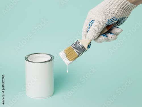 A gloved hand holds a paint brush with white paint.