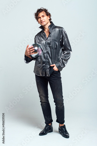 Handsome man posing with a shiny disco ball in studio. © Smile