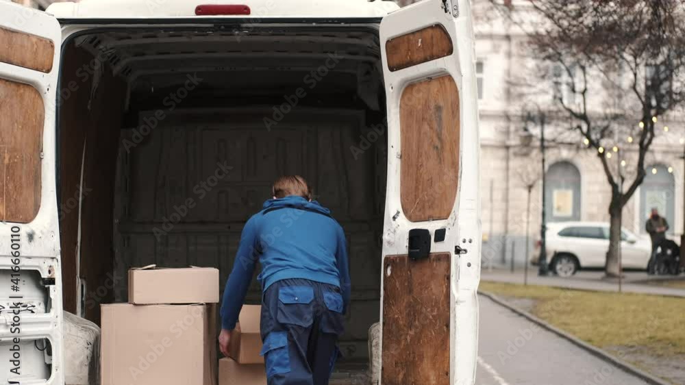 Delivery service. Man carrying boxes, parcels and putting them into white van. Urban background. Delivery service. Man carrying boxes, parcels and putting them into white van. Urban background.