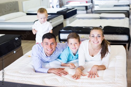 Cheerful family of four choosing right mattress in modern home furnishings shop