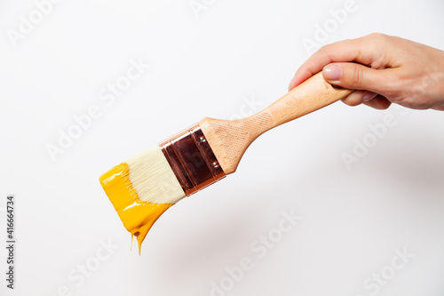 Fototapeta Naklejka Na Ścianę i Meble -  Hand with paintbrush with yellow paint drips off the brush