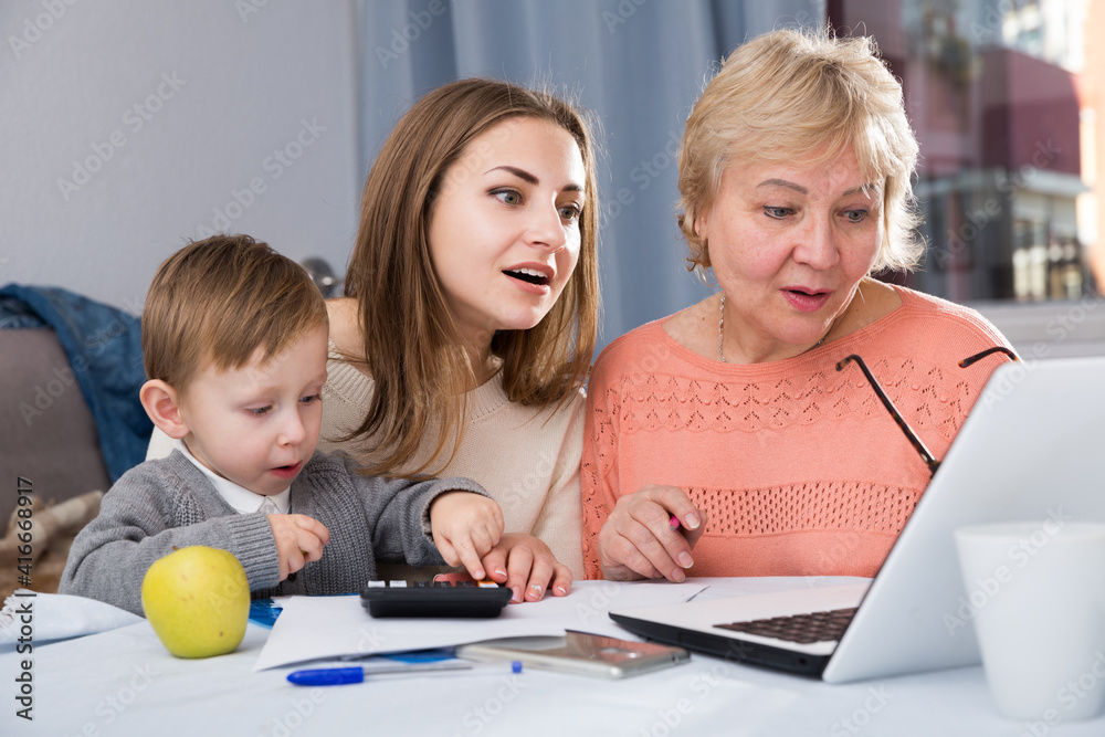 Fototapeta premium Aged woman is mastering technology near laptop with her daughter and grandson at home.