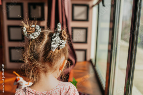 little girl with shaggy hairstyle with two bunches of hair and ribbons stands back in interior of dark room. selective focus