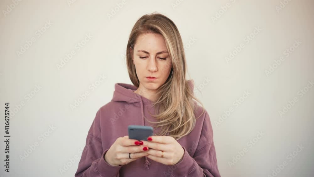 Beautiful blond woman in hoodie busy typing a message on a smartphone over white background. Beautiful blond woman in hoodie busy typing a message on a smartphone over white background.