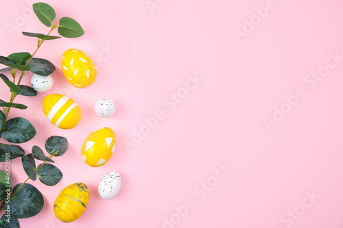 Happy easter concept. Yellow eggs and a branch of eucalyptus on a pink pastel background. Flat lay, top view, copy space.