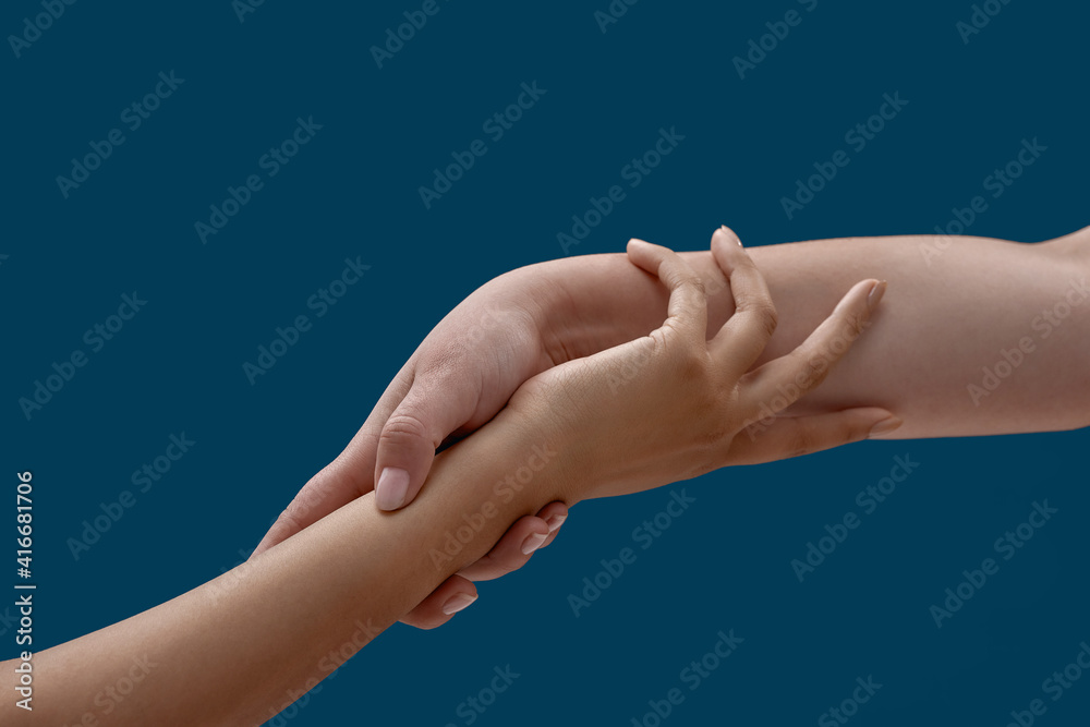 Close up of two women holding each other wrist isolated on blue background