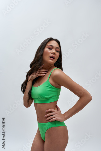 Portrait of sexy young female model with slim body wearing green underwear looking aside, posing for camera isolated over light background © Svitlana
